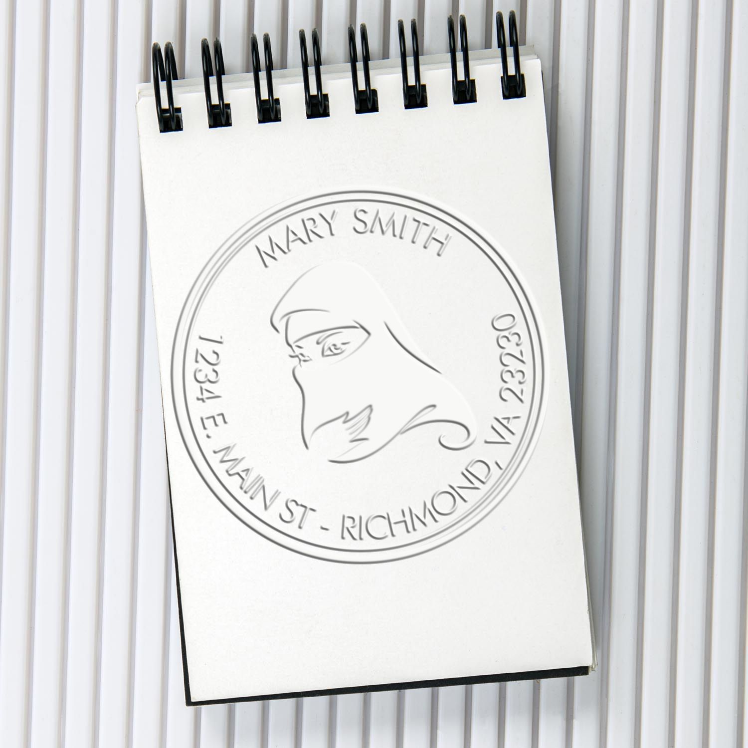 White spiral notepad with embossed custom seal stamp for Mary Smith, black binding clips, on a light gray background.