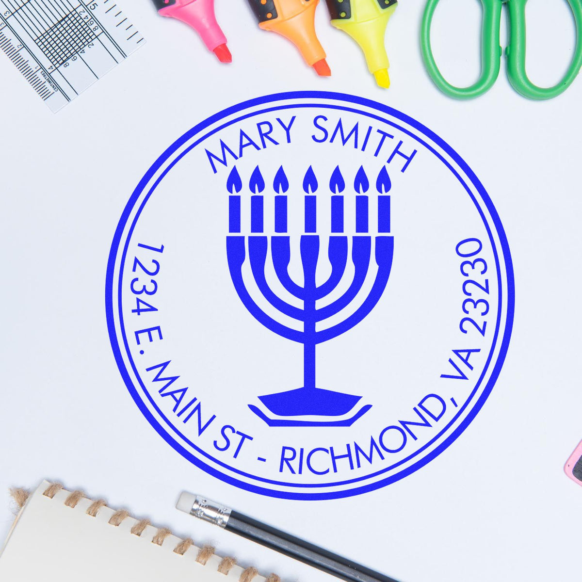Blue custom stamp seal with menorah emblem and Mary Smith text, on a white background with colorful office supplies.