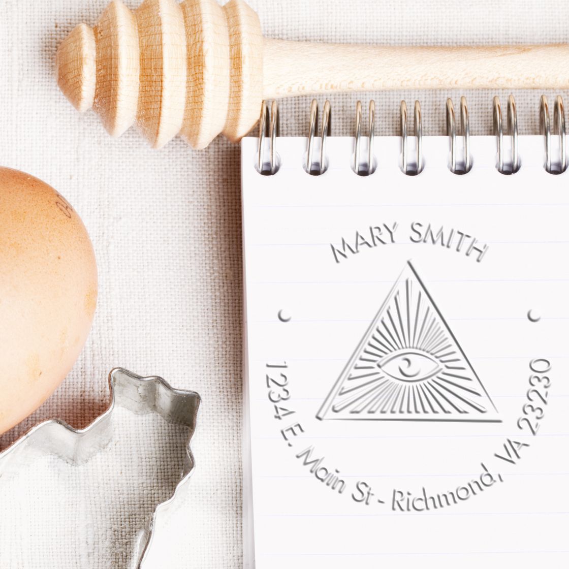 Natural wood stamp and embossed seal on a white spiral notebook, plus a silver seal die on beige fabric.