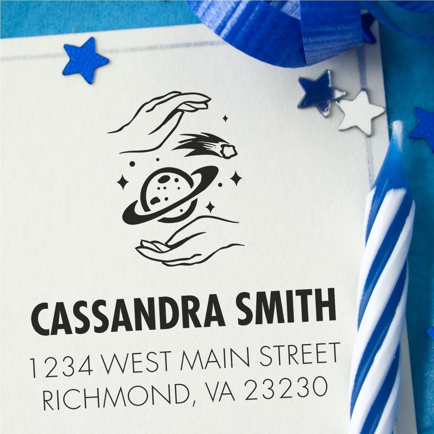 Custom black return address stamp and seal with hands-and-planet graphic, Cassandra Smith, on white card with blue stars and ribbon.