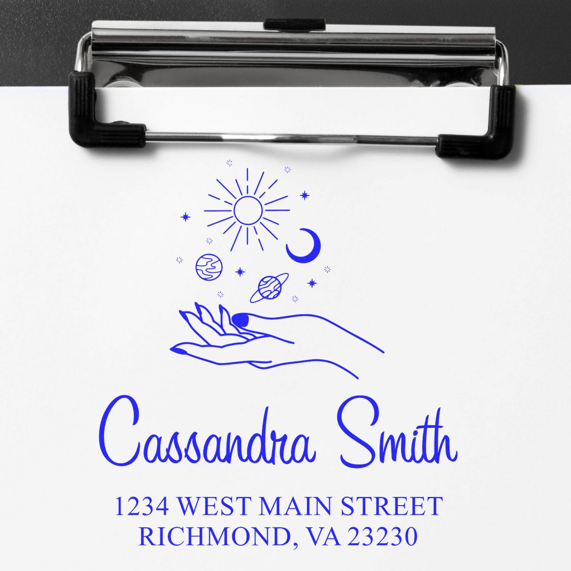 Custom blue stamp seal with hands, sun, moon and stars, showing Cassandra Smith and address on white paper, clipped in black holder.