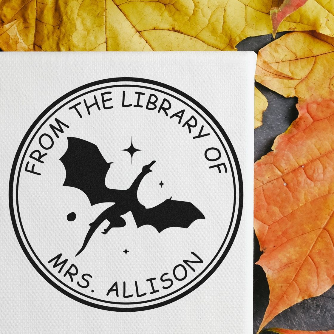 Black circular stamp seal with bat icon and From the Library of Mrs. Allison on white textured paper, with autumn leaves.