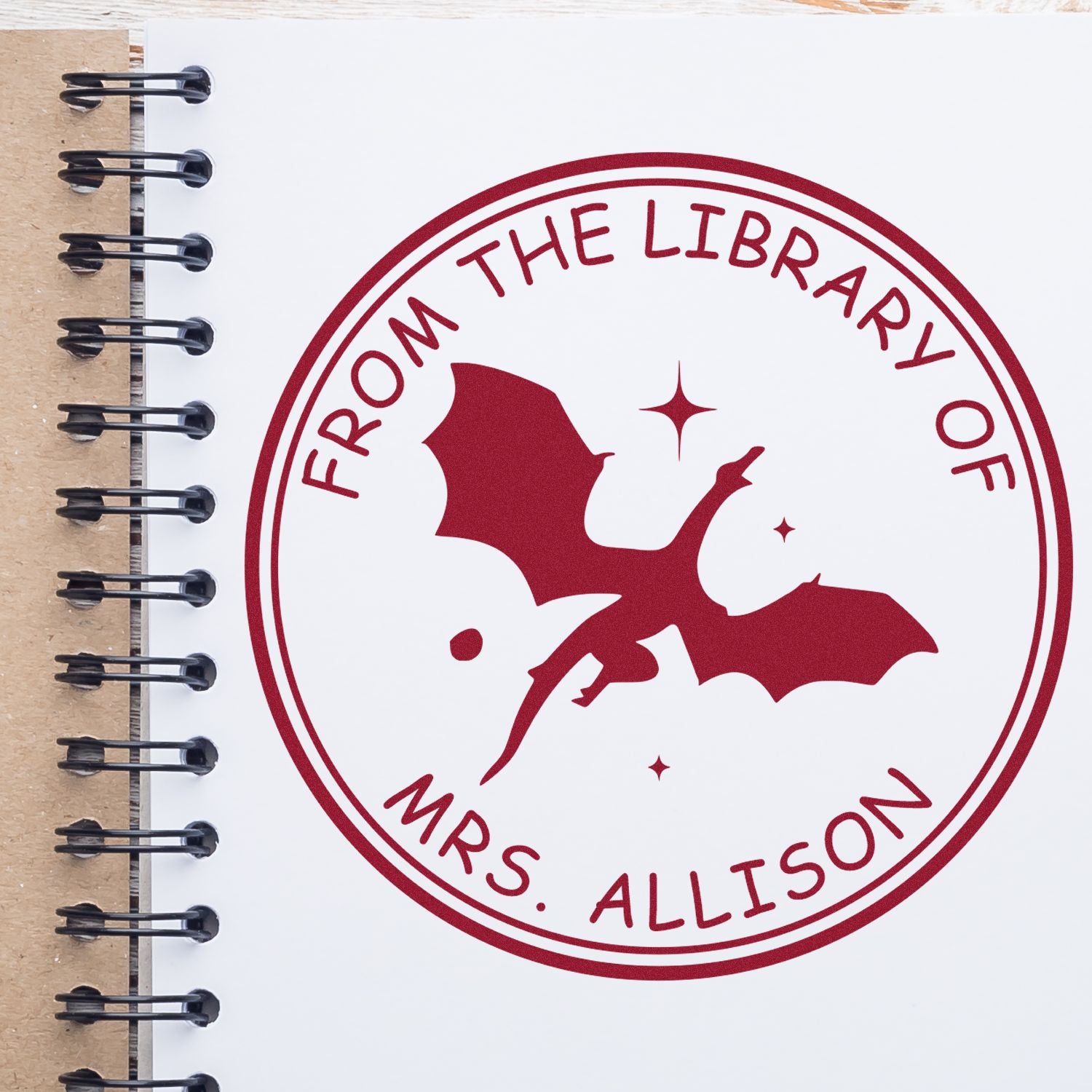 Red custom library stamp seal with bat silhouette and stars on a white notebook page, reading From the Library of Mrs. Allison.