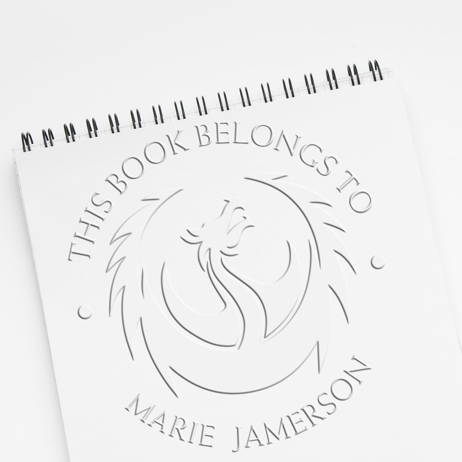 White spiral notebook with embossed book ownership seal stamp, bird emblem, and This Book Belongs to Marie Jamerson.