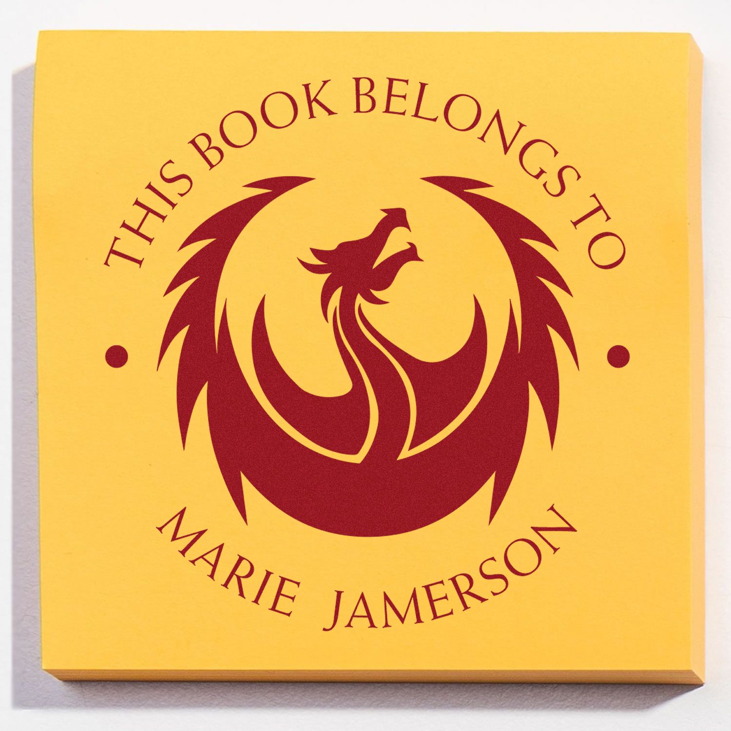 Yellow bookplate stamp seal with maroon phoenix emblem and curved text This Book Belongs to Marie Jamerson.
