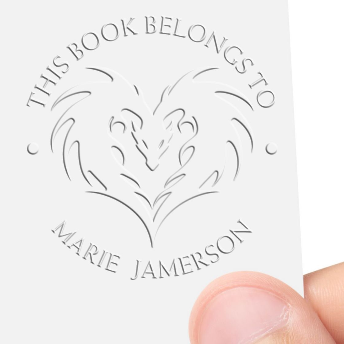 White embossed book ownership seal stamp with heart monogram and curved text, This Book Belongs to Marie Jamerson