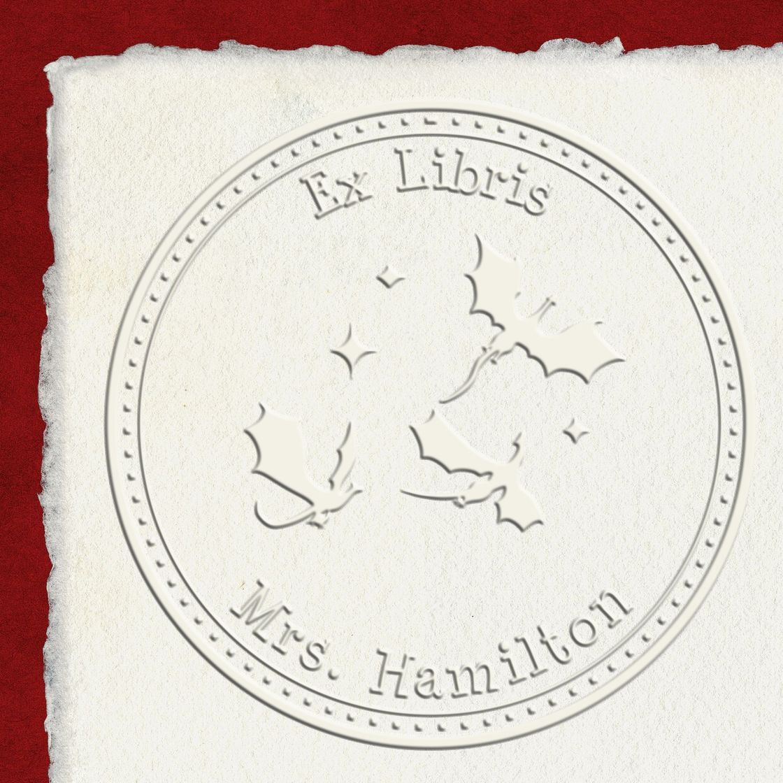 Embossed white circular bookplate stamp seal reading Ex Libris Mrs. Hamilton with textured paper on deep red background.