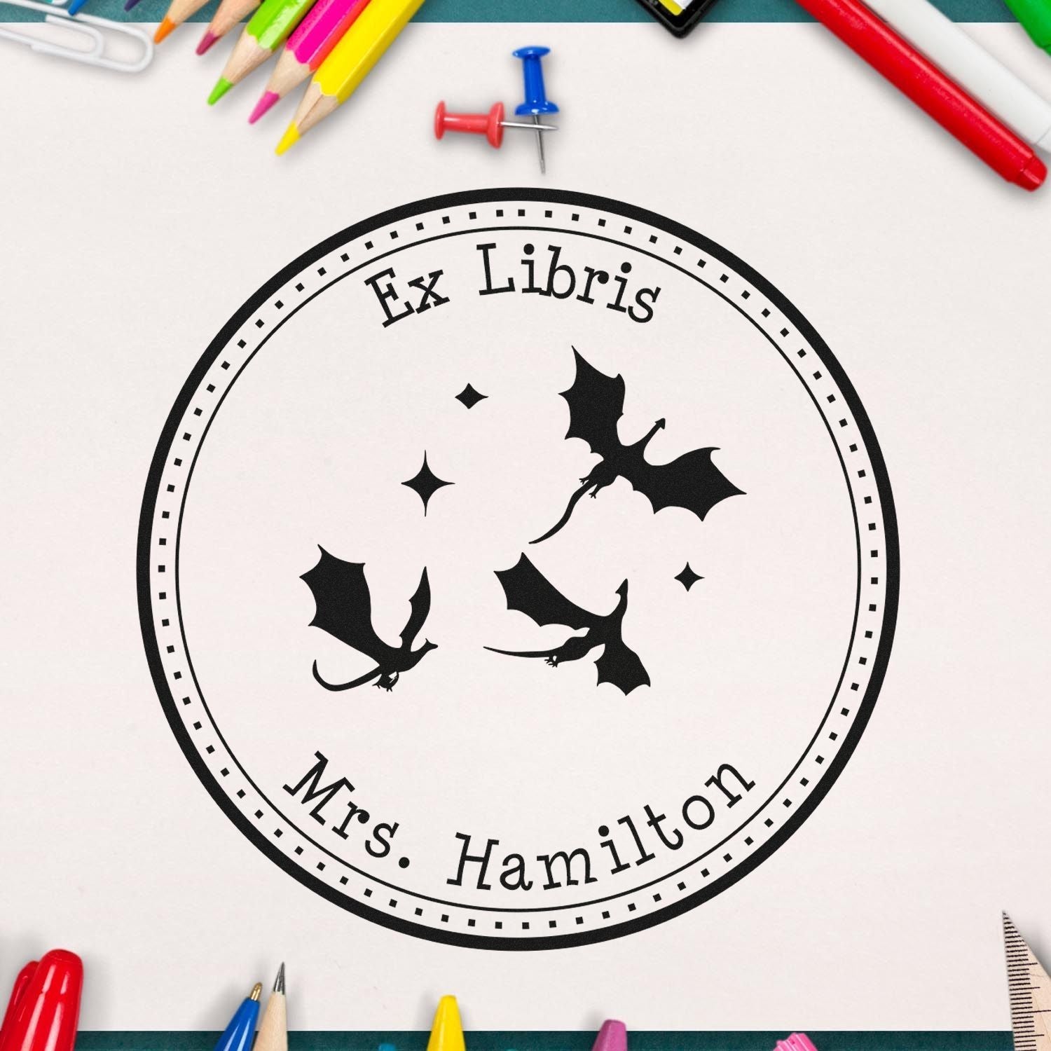 Round black Ex Libris library stamp seal with three dragons and Mrs. Hamilton, on white with colorful pencils.
