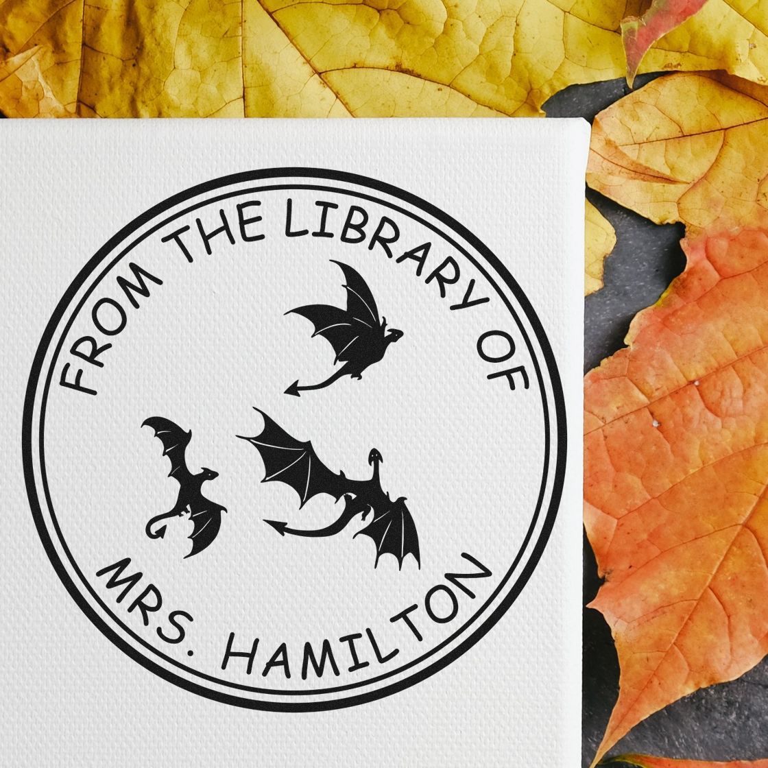 Black circular stamp seal with bats and From the Library of Mrs. Hamilton on white paper, framed by yellow-orange leaves.