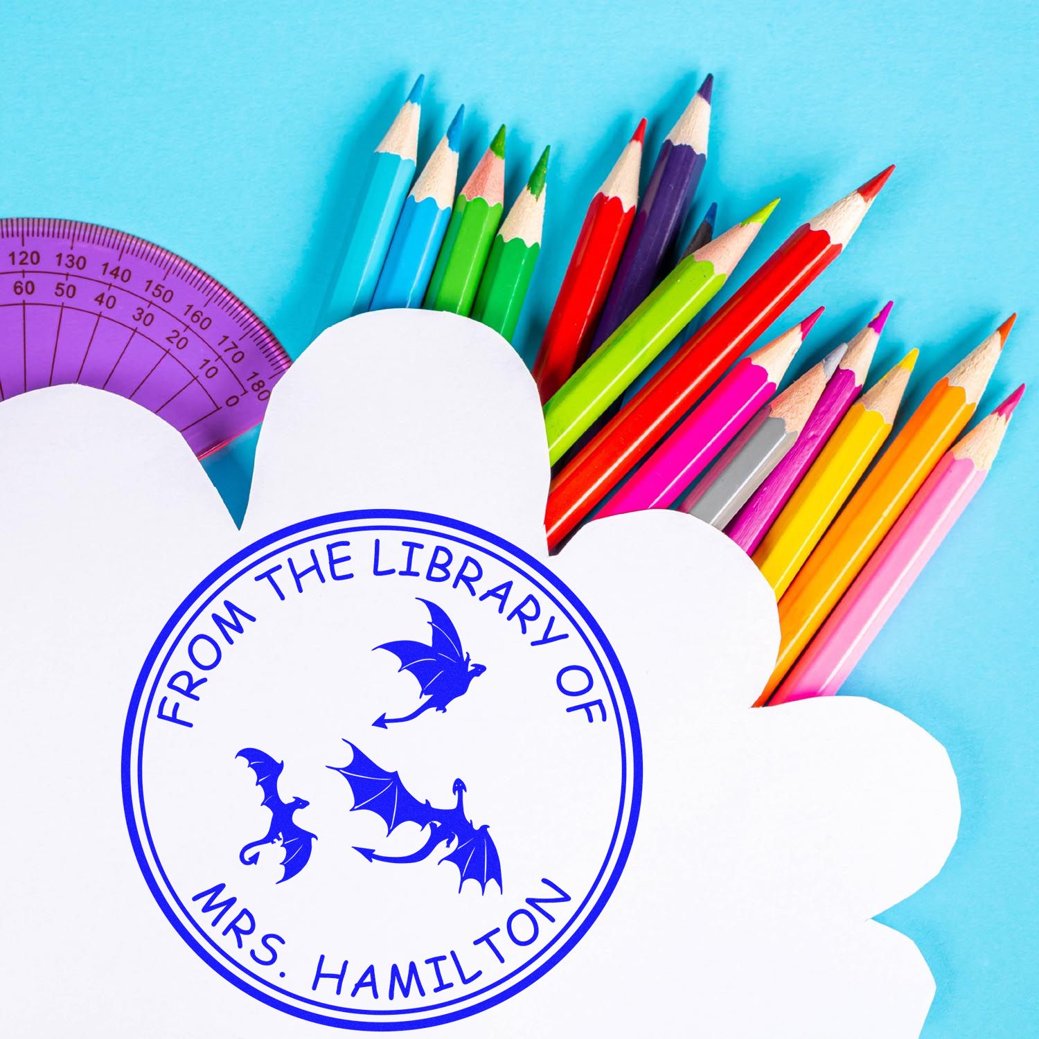 Custom blue library stamp seal on white paper with colorful pencils, purple protractor, and dragon design on blue background.