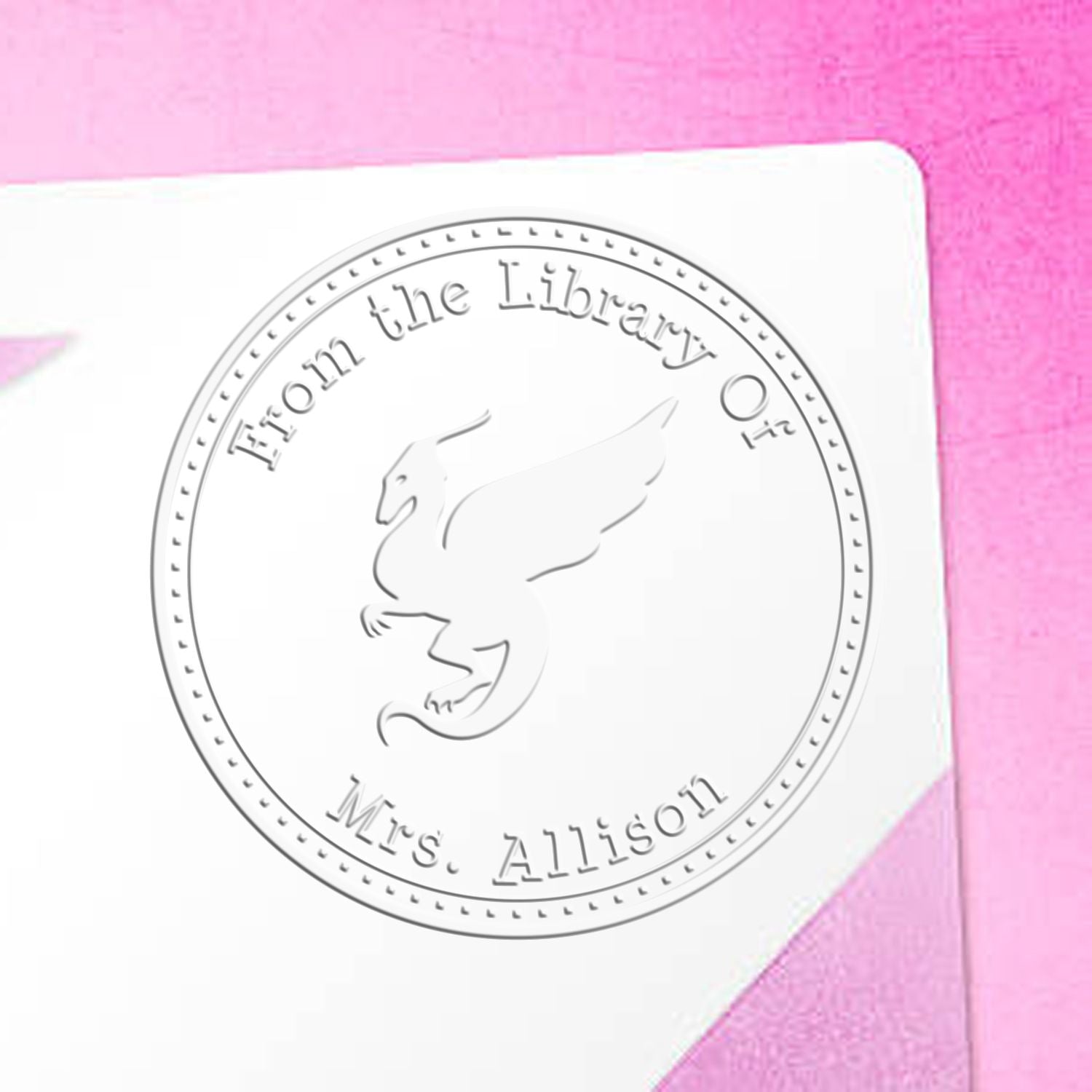 Custom embossed library seal on white card with winged lion emblem, reading From the Library of Mrs. Allison, on pink background.