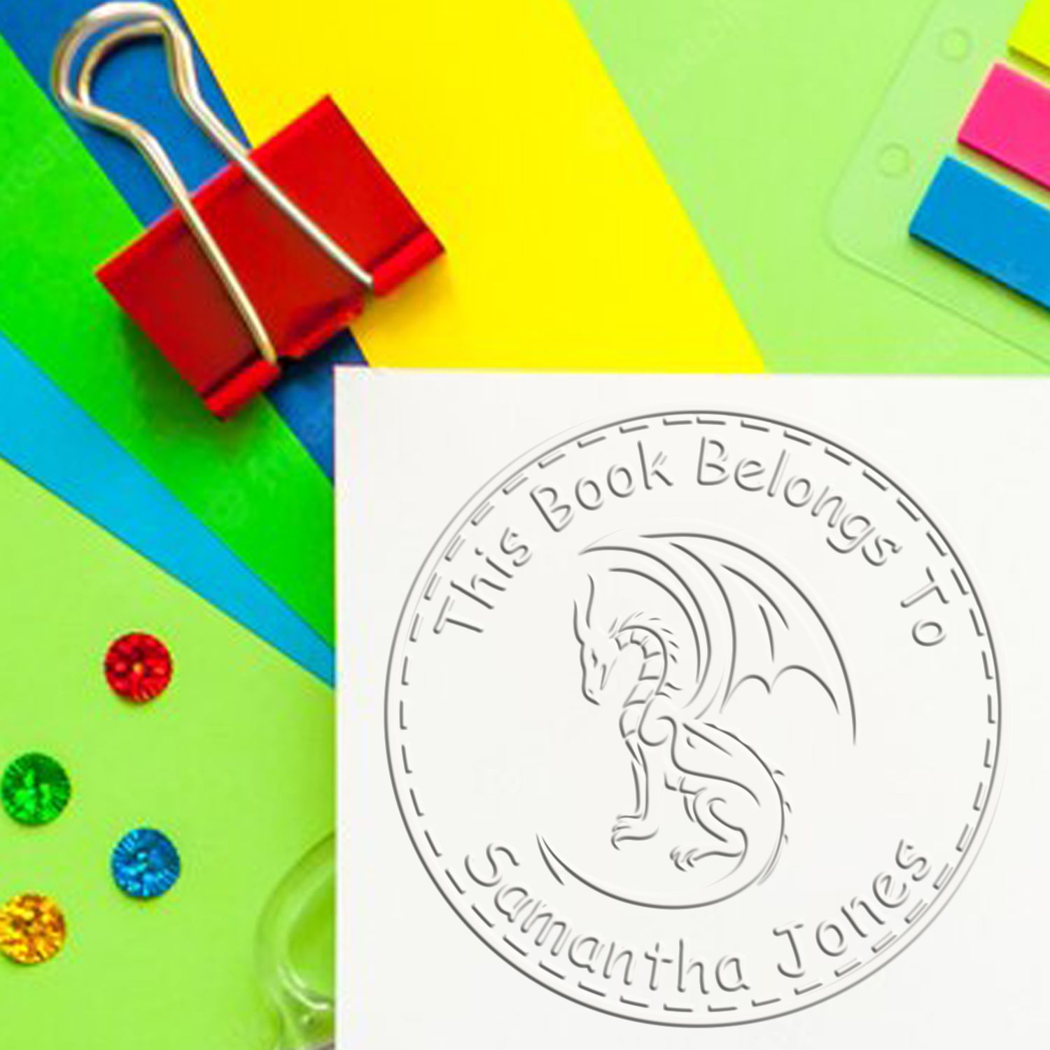 Colorful stamp and seal products with a white embossed dragon bookplate seal reading This Book Belongs to Samantha Jones.