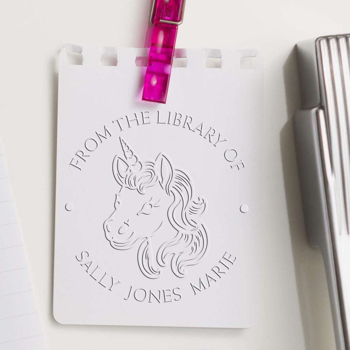 White unicorn library stamp seal with pink clip and silver tool, embossed with From the Library of Sally Jones Marie.