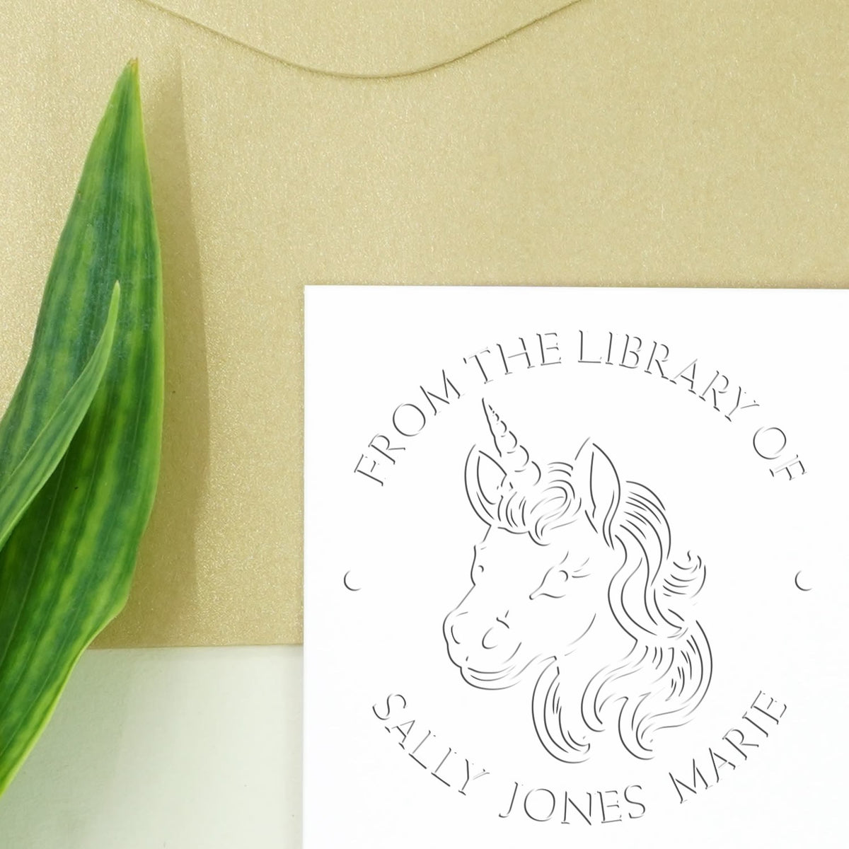 White custom library stamp seal with unicorn line art on beige background, accented by a green leaf