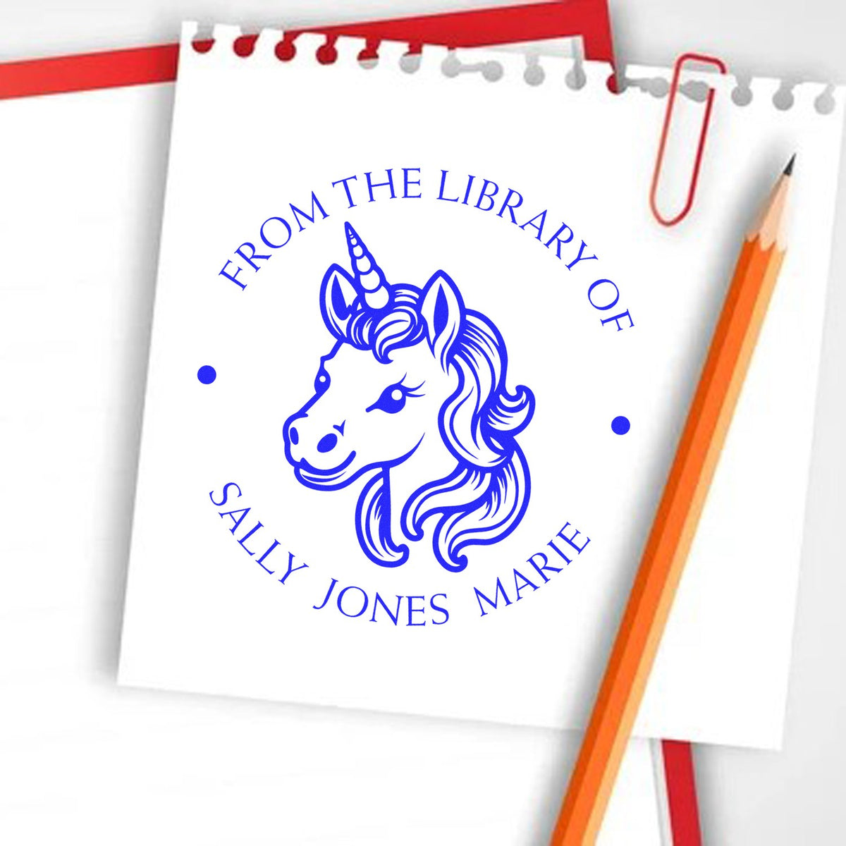 Blue unicorn library stamp seal reading From the Library of Sally Jones Marie on white paper, with red paperclip and orange pencil.