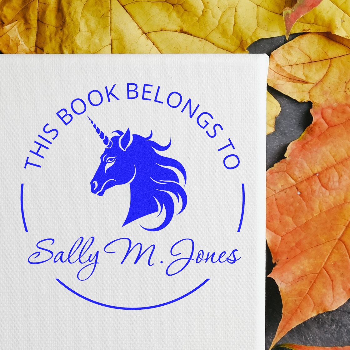 Blue unicorn book stamp/seal for Sally M. Jones on white textured card with autumn leaves.