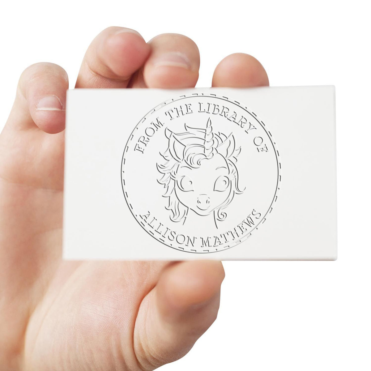Hand holding white custom library stamp card with embossed circular unicorn seal and black text, From the Library of Allison Matthews