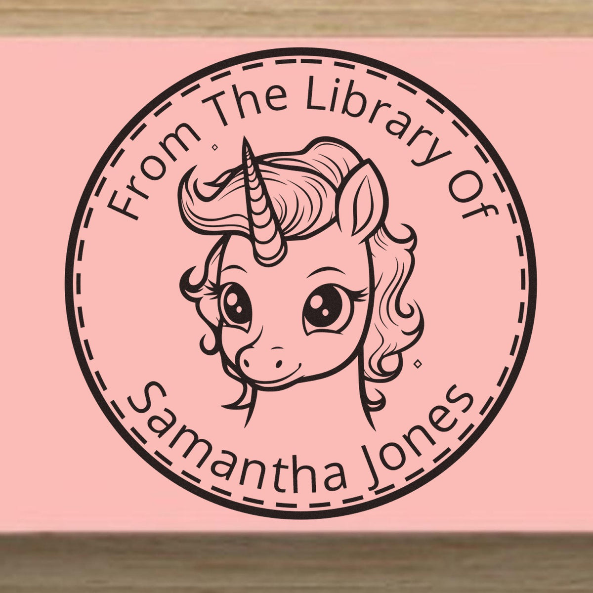 Custom black circular library stamp seal with unicorn and From The Library Of Samantha Jones on a pink background.