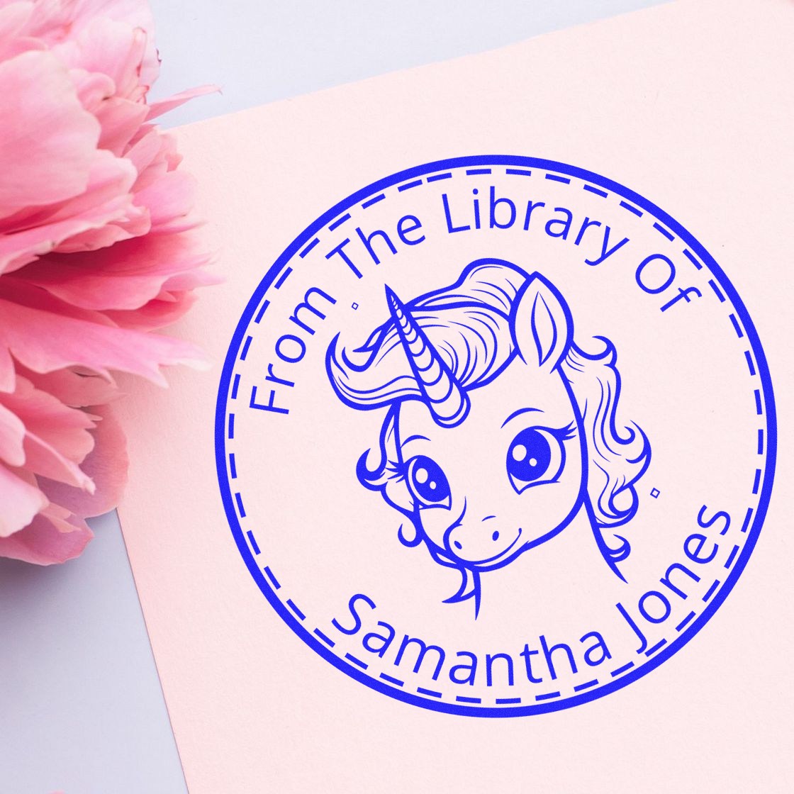 Blue circular custom stamp seal with unicorn and Samantha Jones text on pale pink paper, beside pink flowers.
