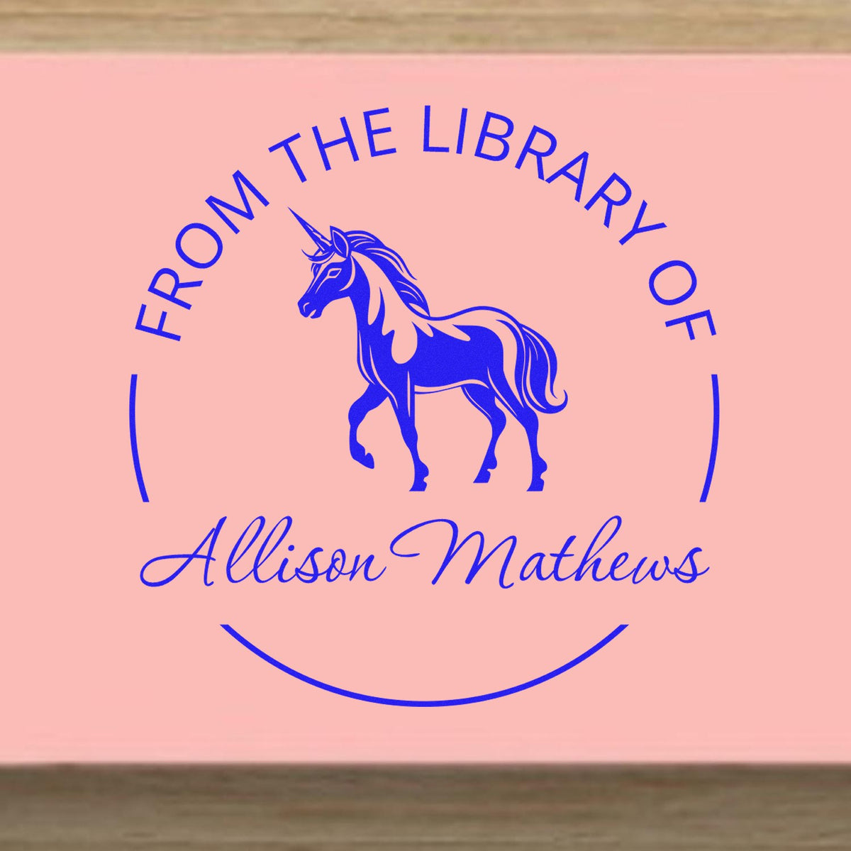 Pink custom library stamp seal with a blue unicorn, arched text, and Allison Mathews in script.