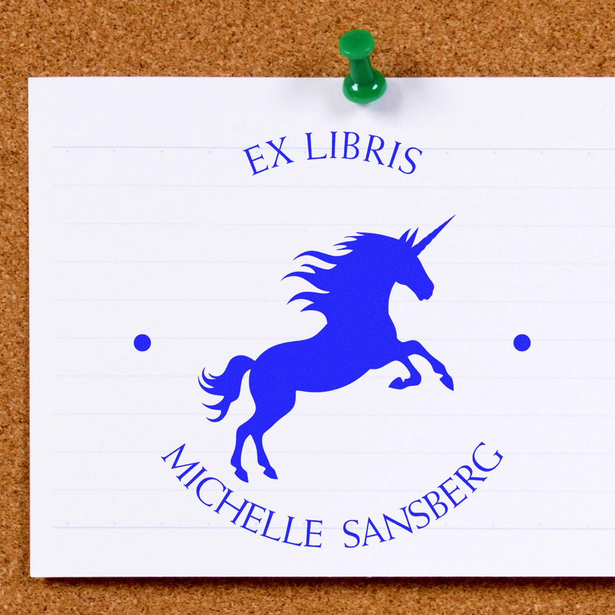 Blue unicorn ex libris book stamp seal on white paper, pinned to a corkboard with a green pushpin.