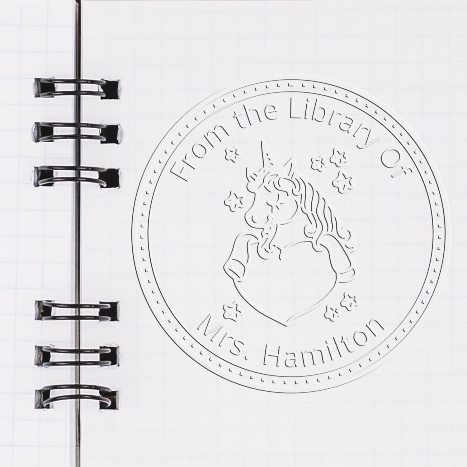 Silver embossed unicorn library stamp and seal for Mrs. Hamilton on white notebook page with black spiral binding