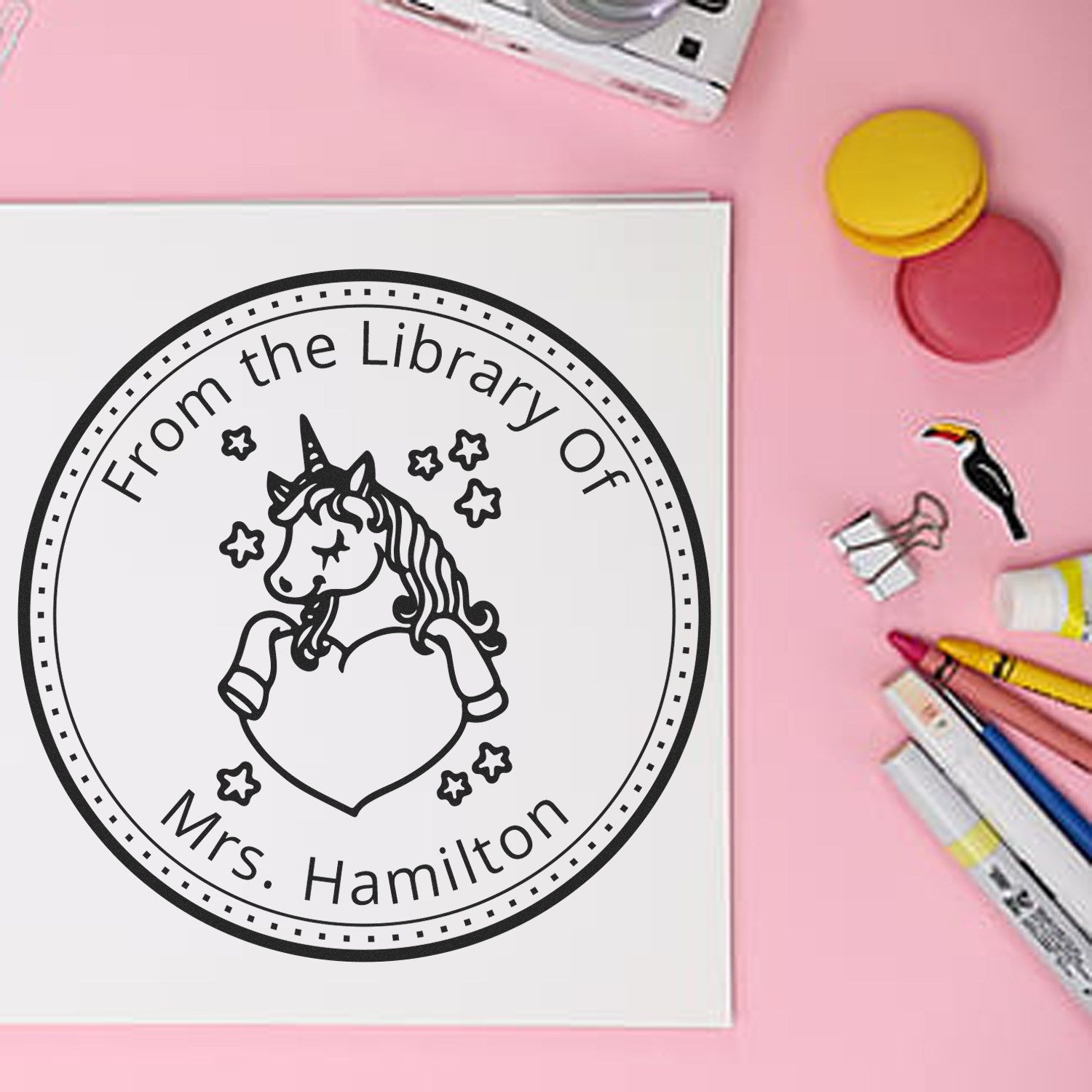 Custom black unicorn library stamp seal on white card, on a pink background with yellow and pink seal caps and pens.