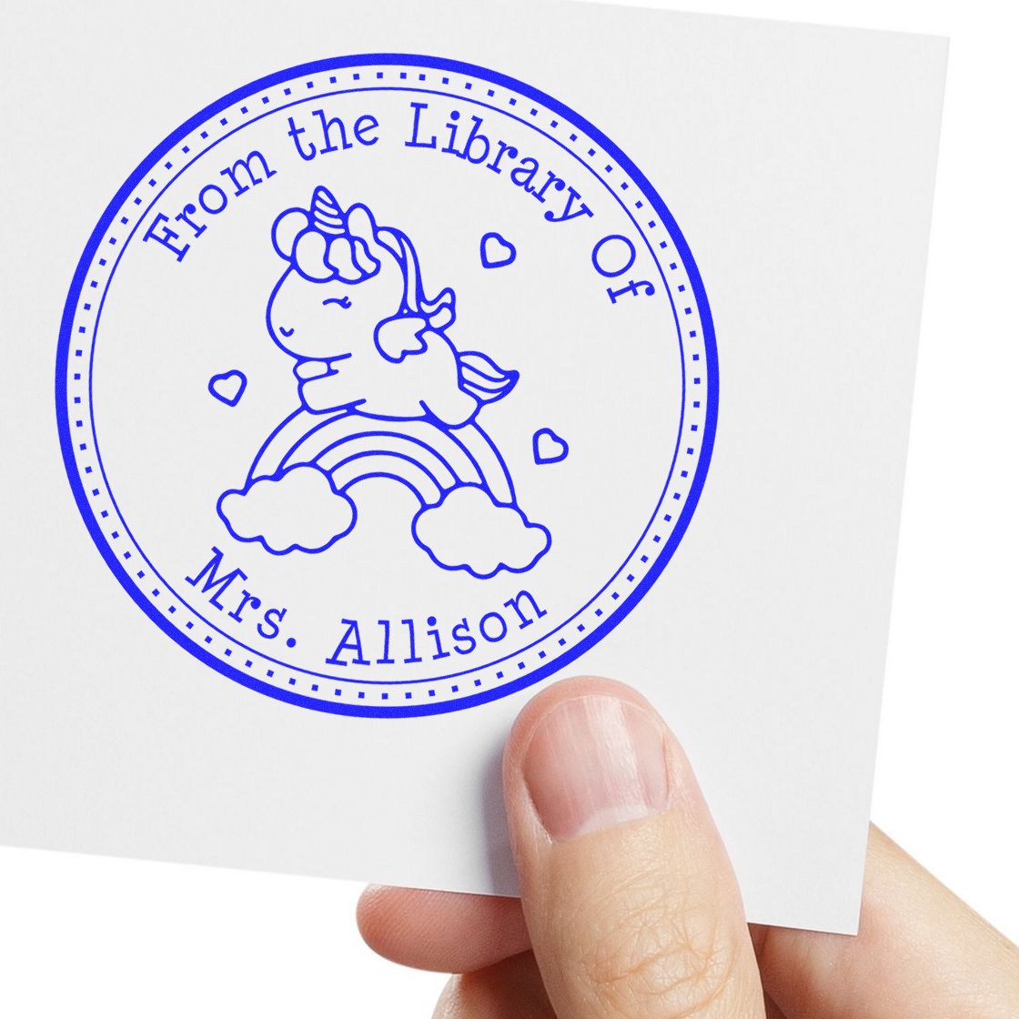 Blue circular book stamp seal with unicorn on rainbow, hearts, and From the Library Of Mrs. Allison on white card.