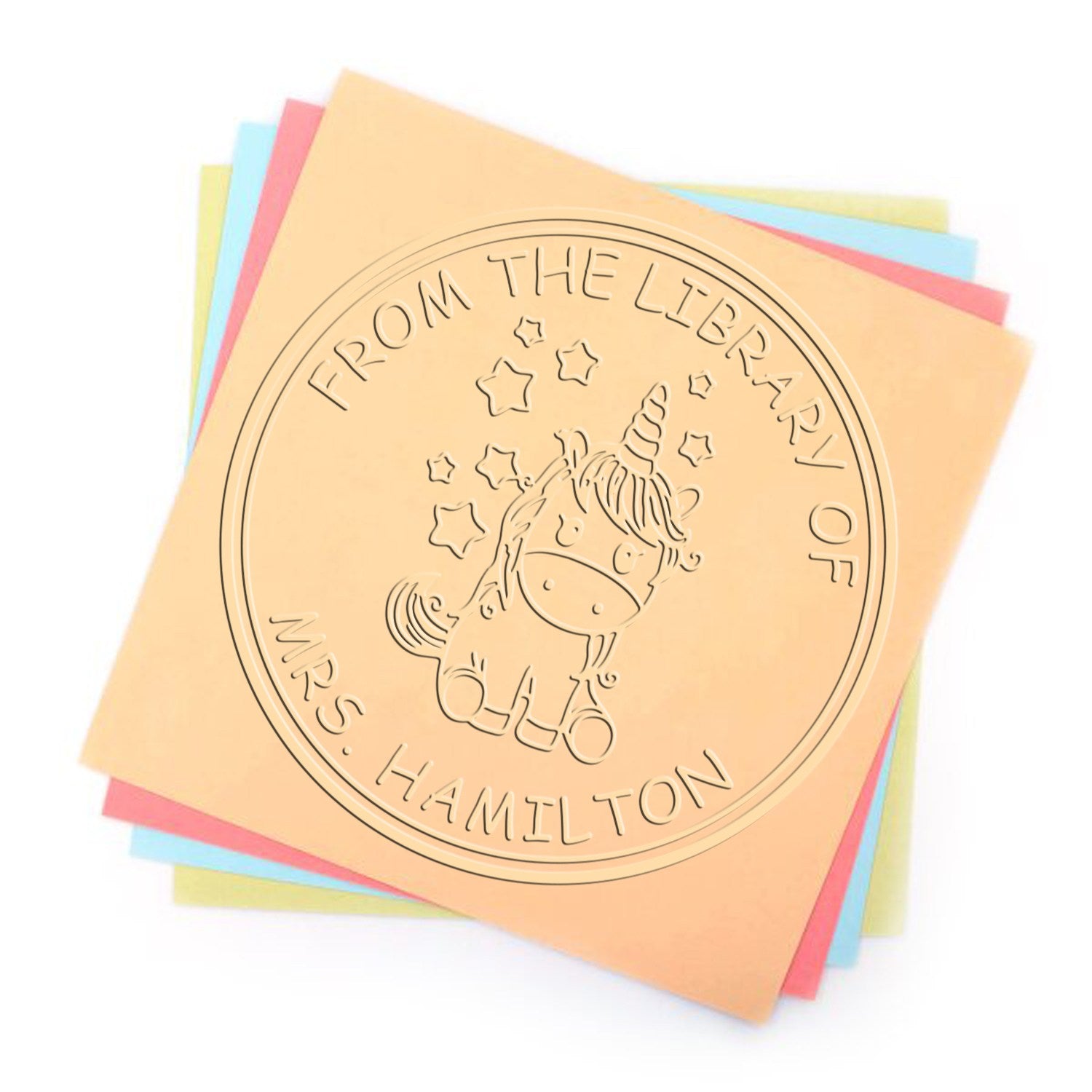 Round embossed unicorn library stamp seal on layered peach, pink, blue, and yellow sheets