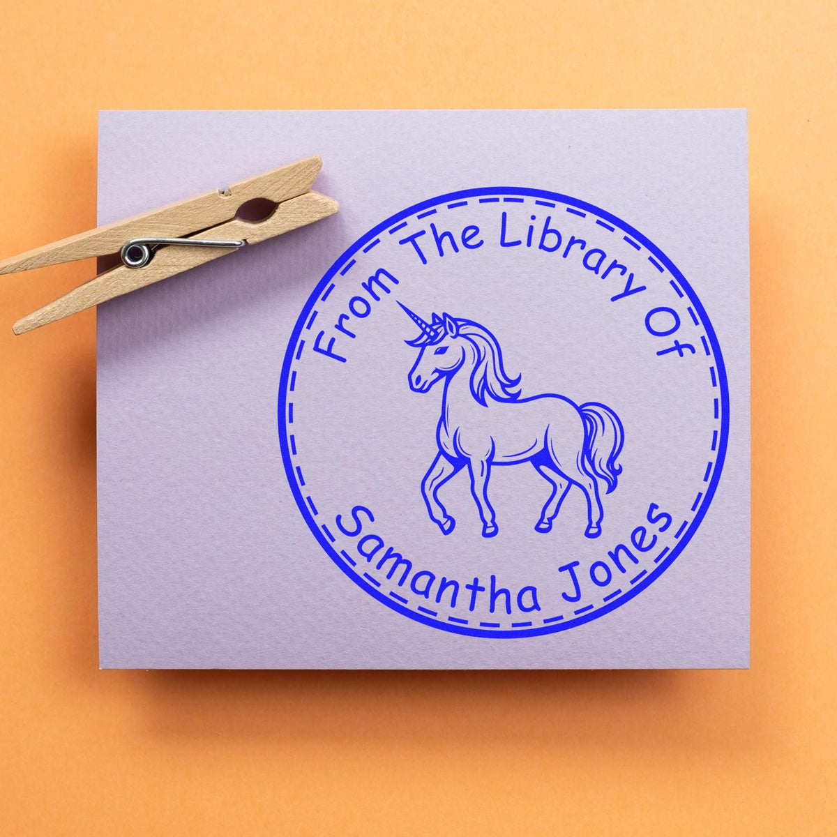 Custom blue unicorn library stamp seal on lavender card with wooden clothespin.