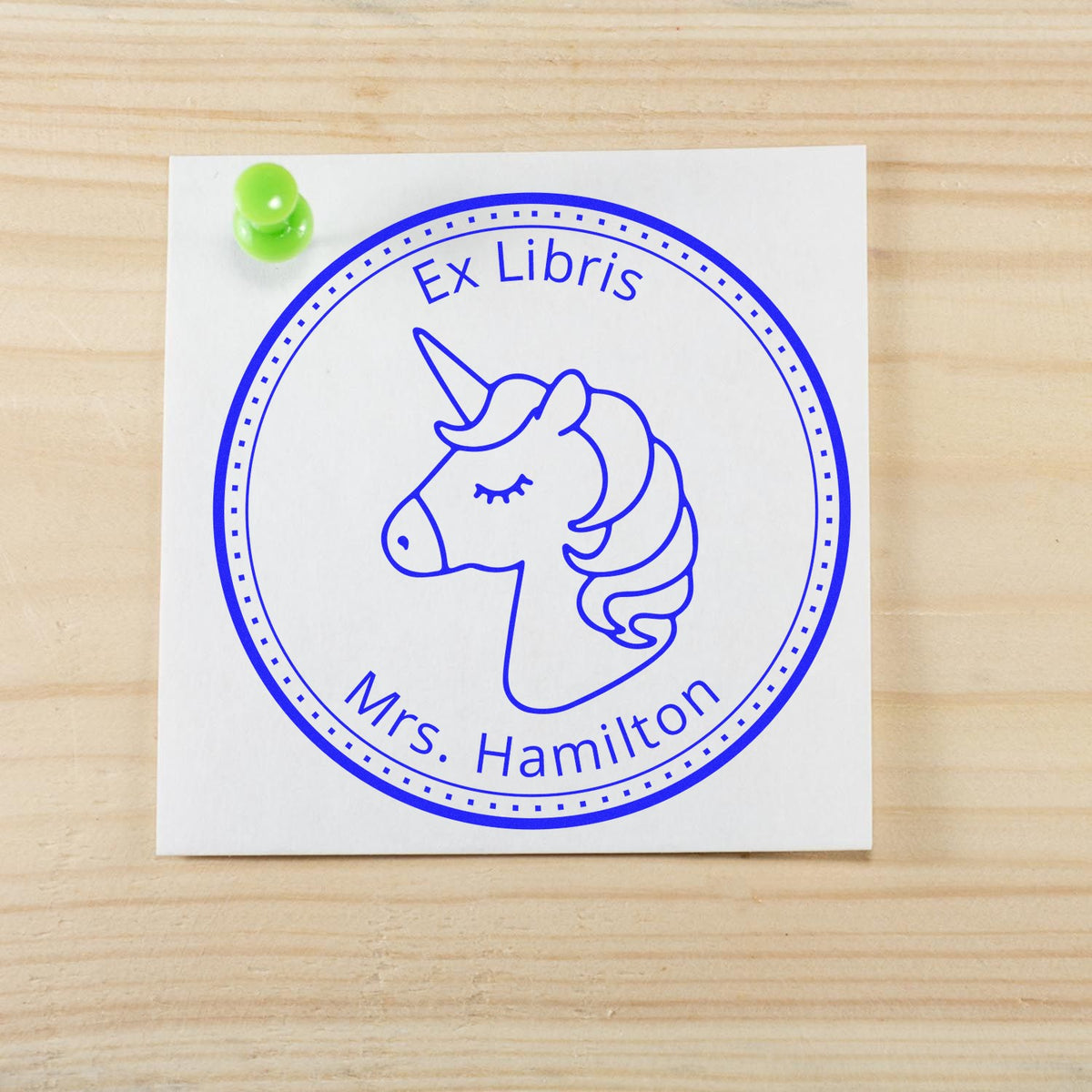 Blue Ex Libris unicorn stamp seal for Mrs. Hamilton on white paper, pinned with green pushpin against a wood background
