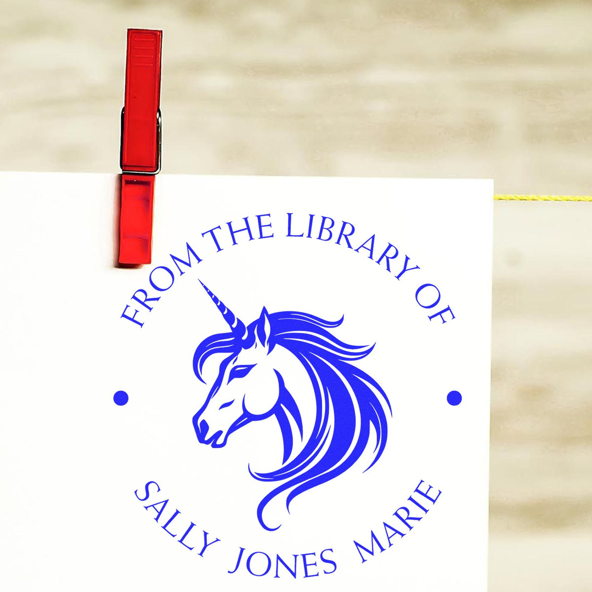 Red stamp clip holding a white sheet with a blue unicorn library seal and circular Sally Jones Marie text.