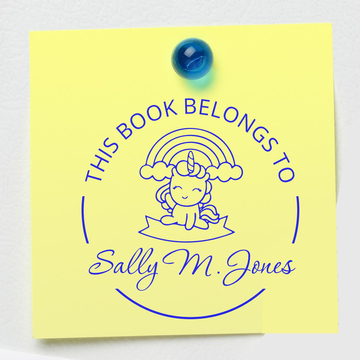 Yellow custom bookplate stamp and seal with blue unicorn, This Book Belongs to Sally M. Jones, pinned with blue tack.