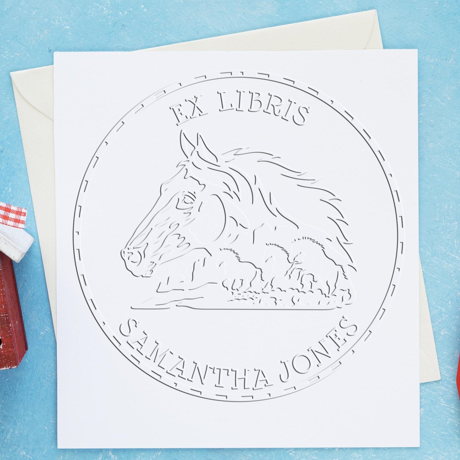 White embossed stamp seal with horse illustration and FX Libris Samantha Jones on a card, on a blue background with envelope.