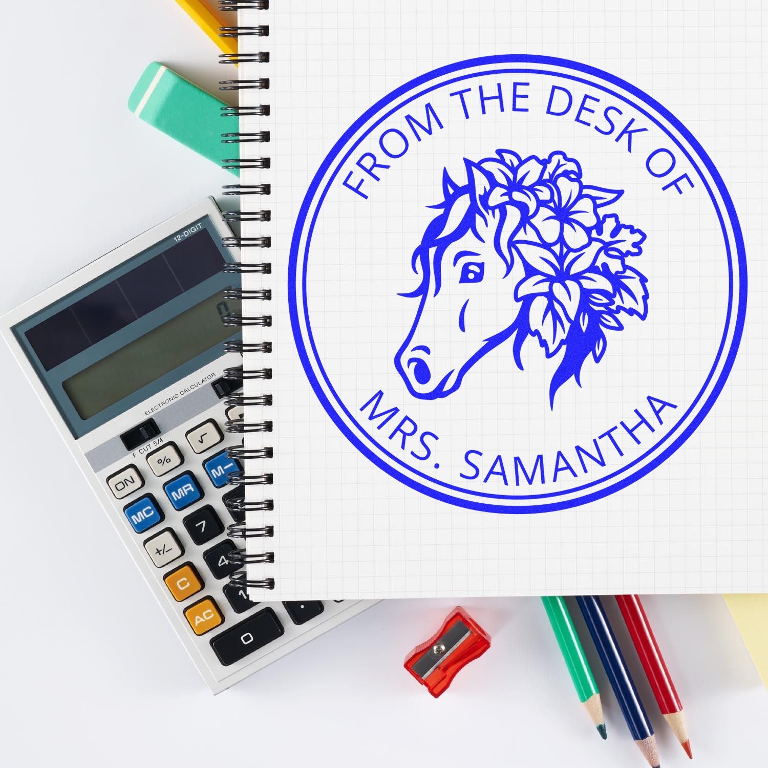 Blue custom stamp seal with horse logo and From the Desk of Mrs. Samantha on a notebook, beside a calculator and pencils.