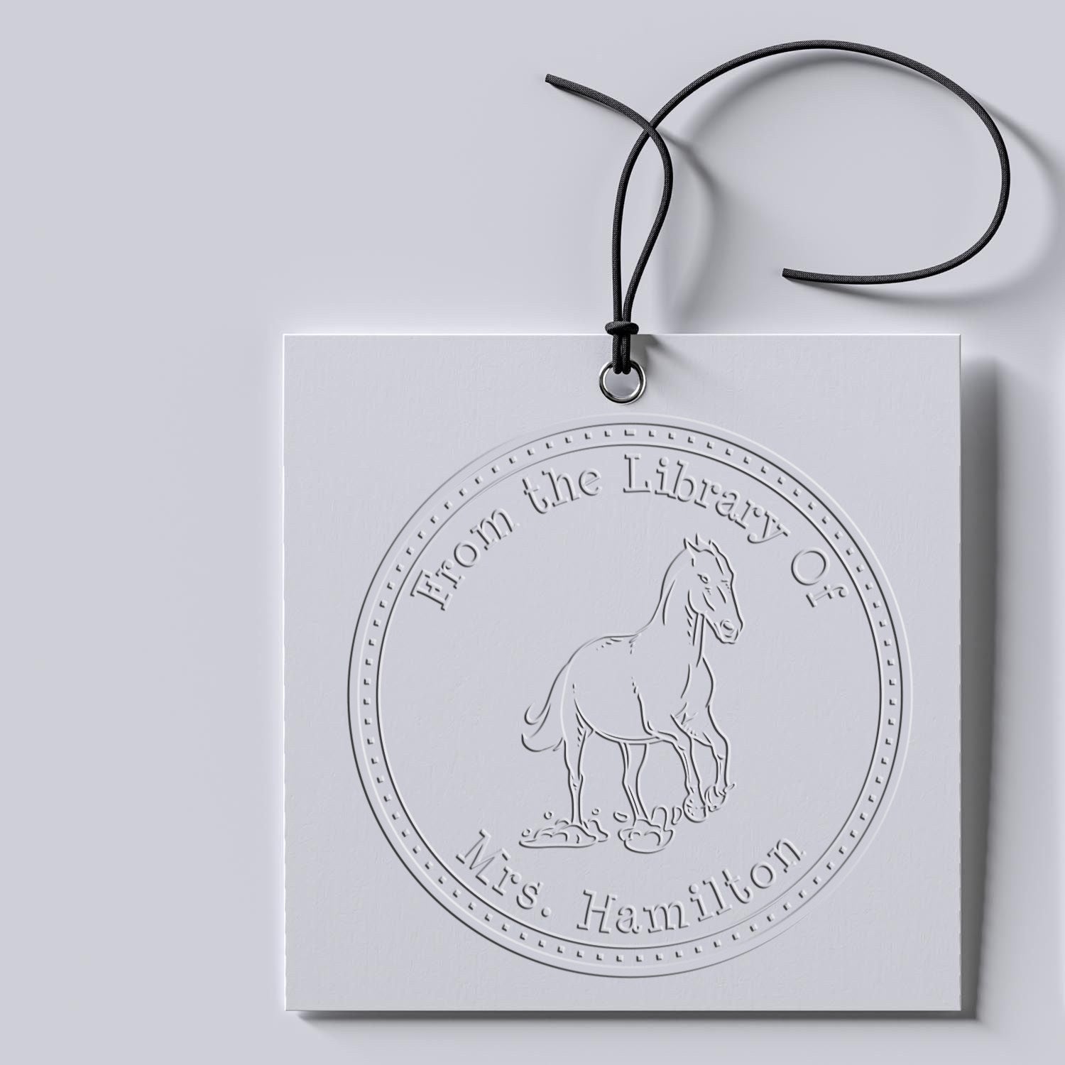 Custom white embossed hanging seal stamp with horse emblem and black cord on light gray background, labeled 'From the Library Of Mrs. Hamilton'.