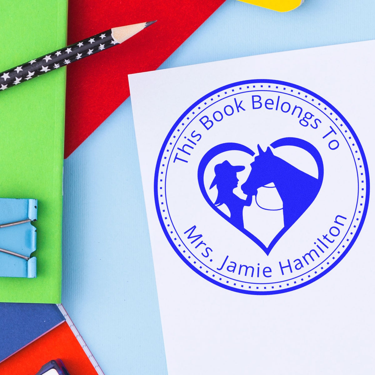 Blue custom book ownership stamp and seal for Mrs. Jamie Hamilton with horse-and-rider heart logo on white paper.