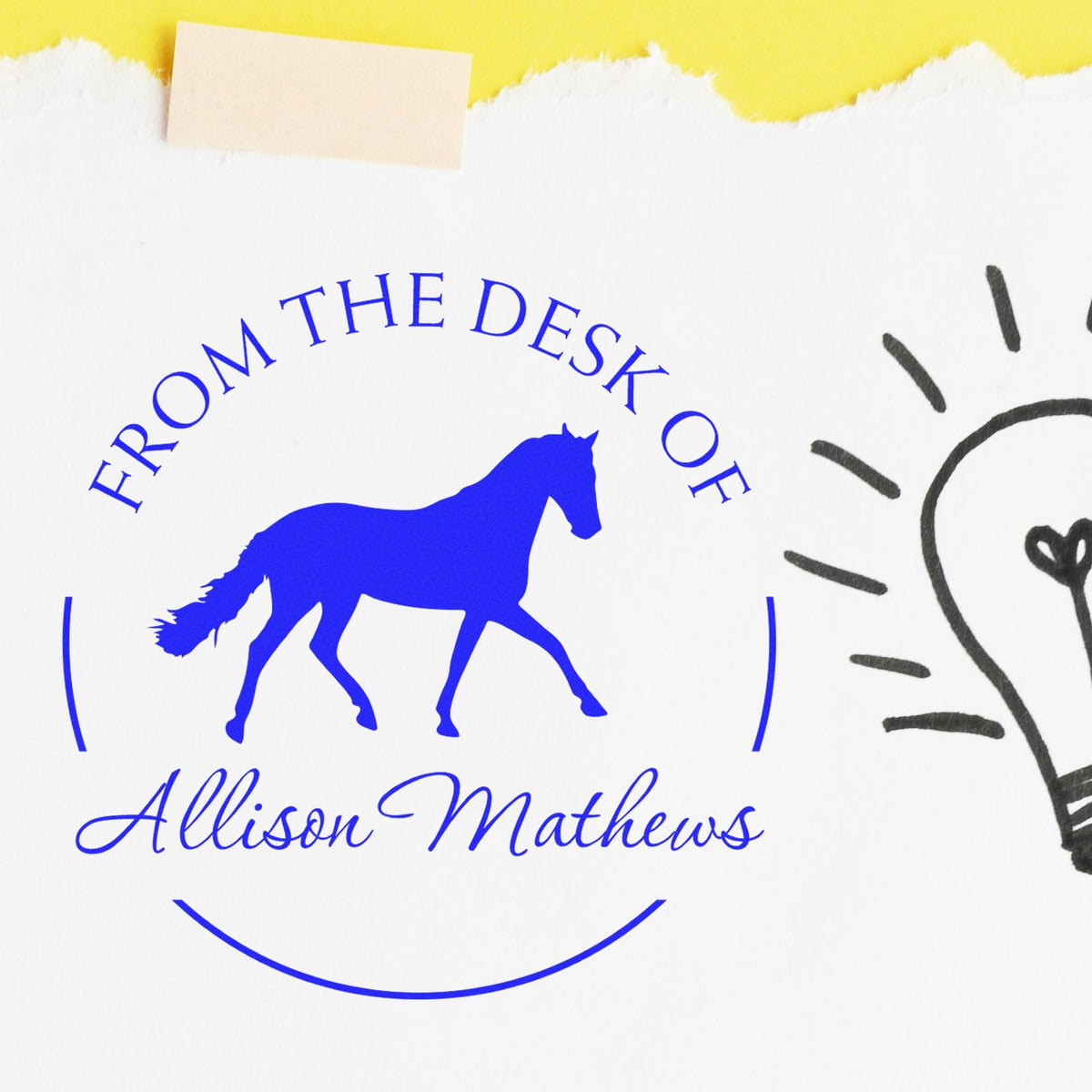Blue custom stamp seal with horse logo and From the Desk of Allison Mathews on white paper with yellow torn edge.