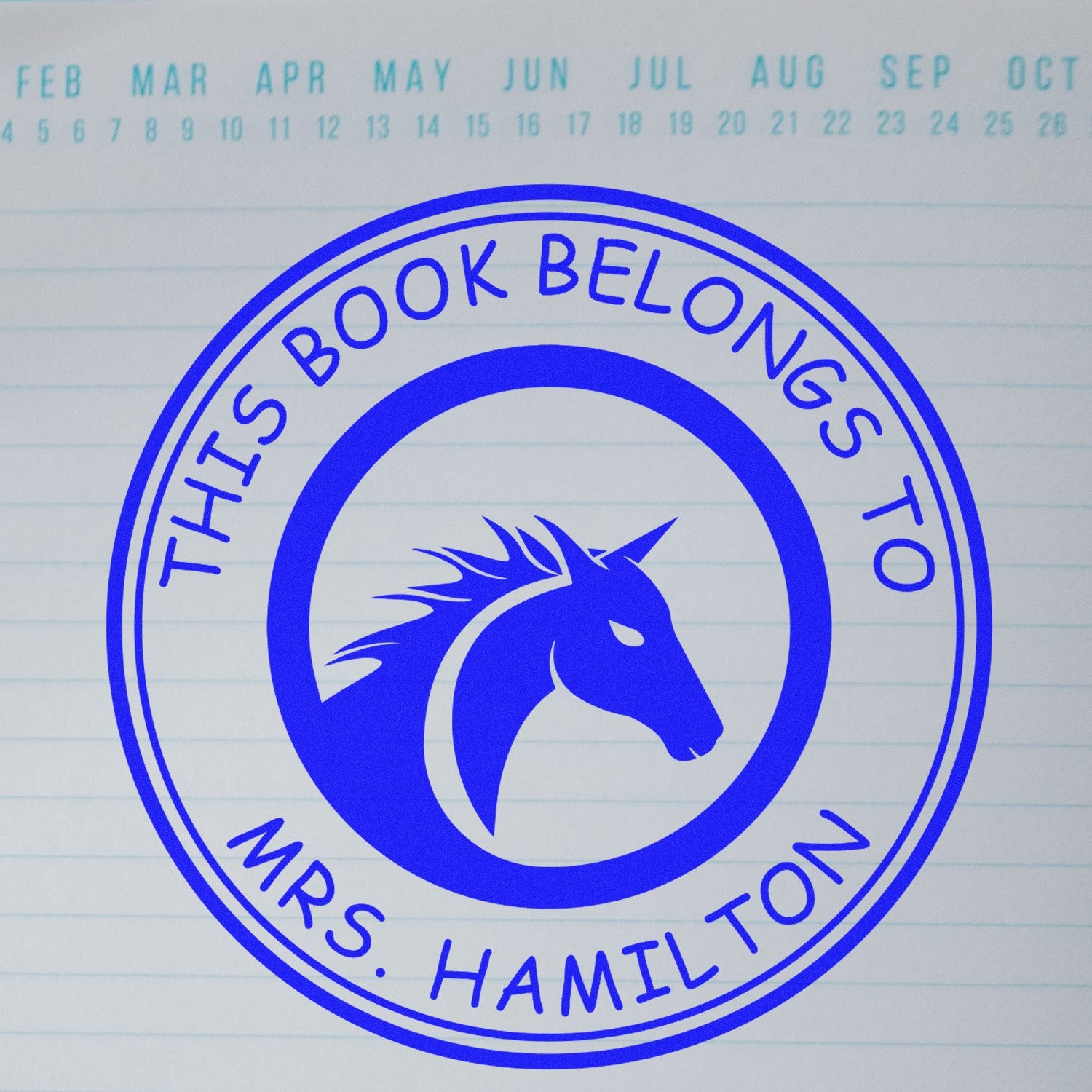 Blue circular custom stamp seal with horse head logo and This Book Belongs to Mrs. Hamilton on lined paper.