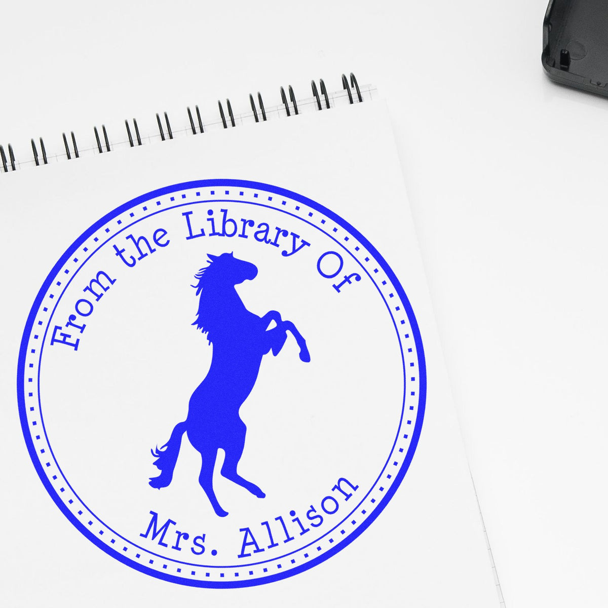 Blue custom library stamp seal on white spiral notebook, featuring a rearing horse silhouette and From the Library Of Mrs. Allison