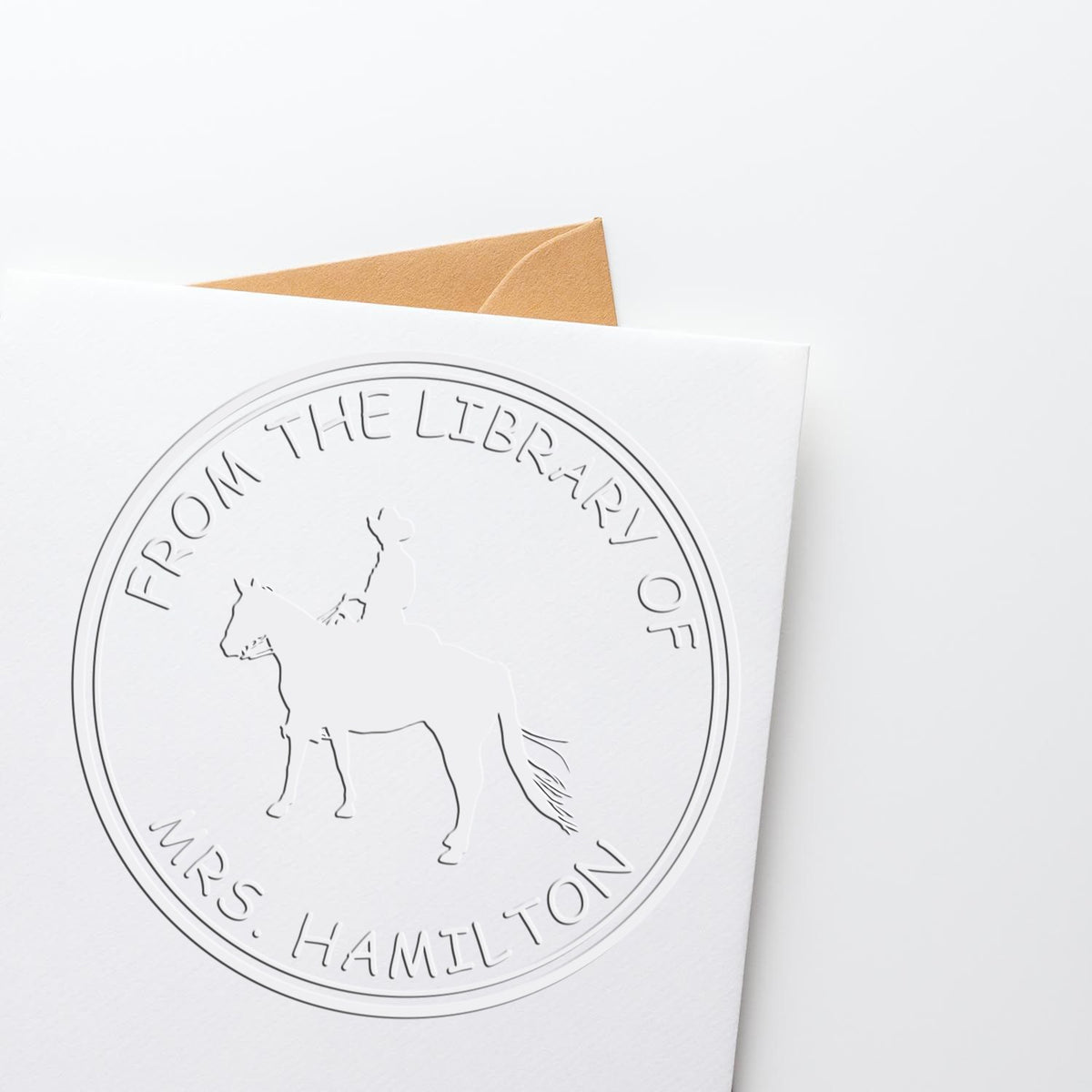 Embossed white library seal stamp reading From the Library of Mrs. Hamilton with horse emblem and tan envelope.