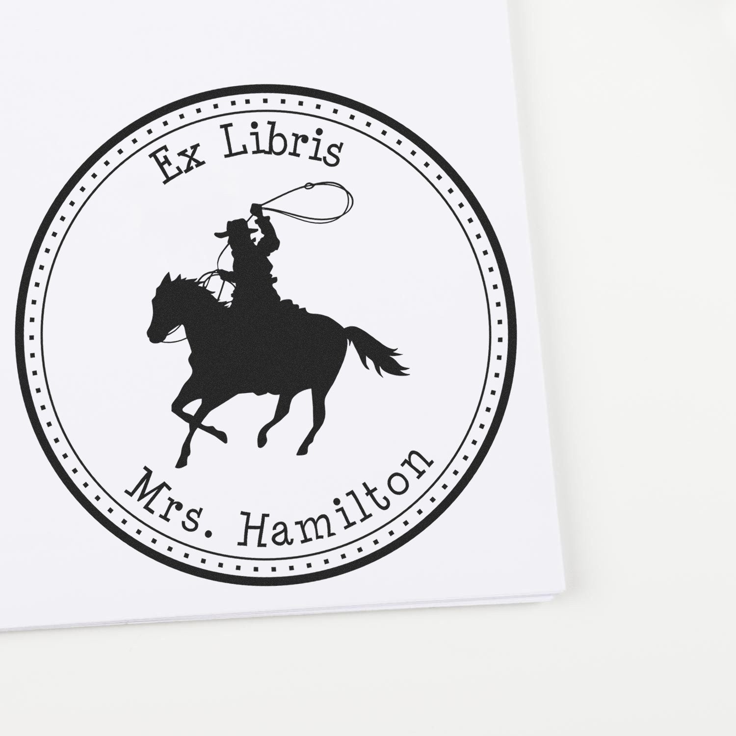 Black circular Ex Libris book stamp seal with cowboy on horse and personalized text "Mrs. Hamilton".