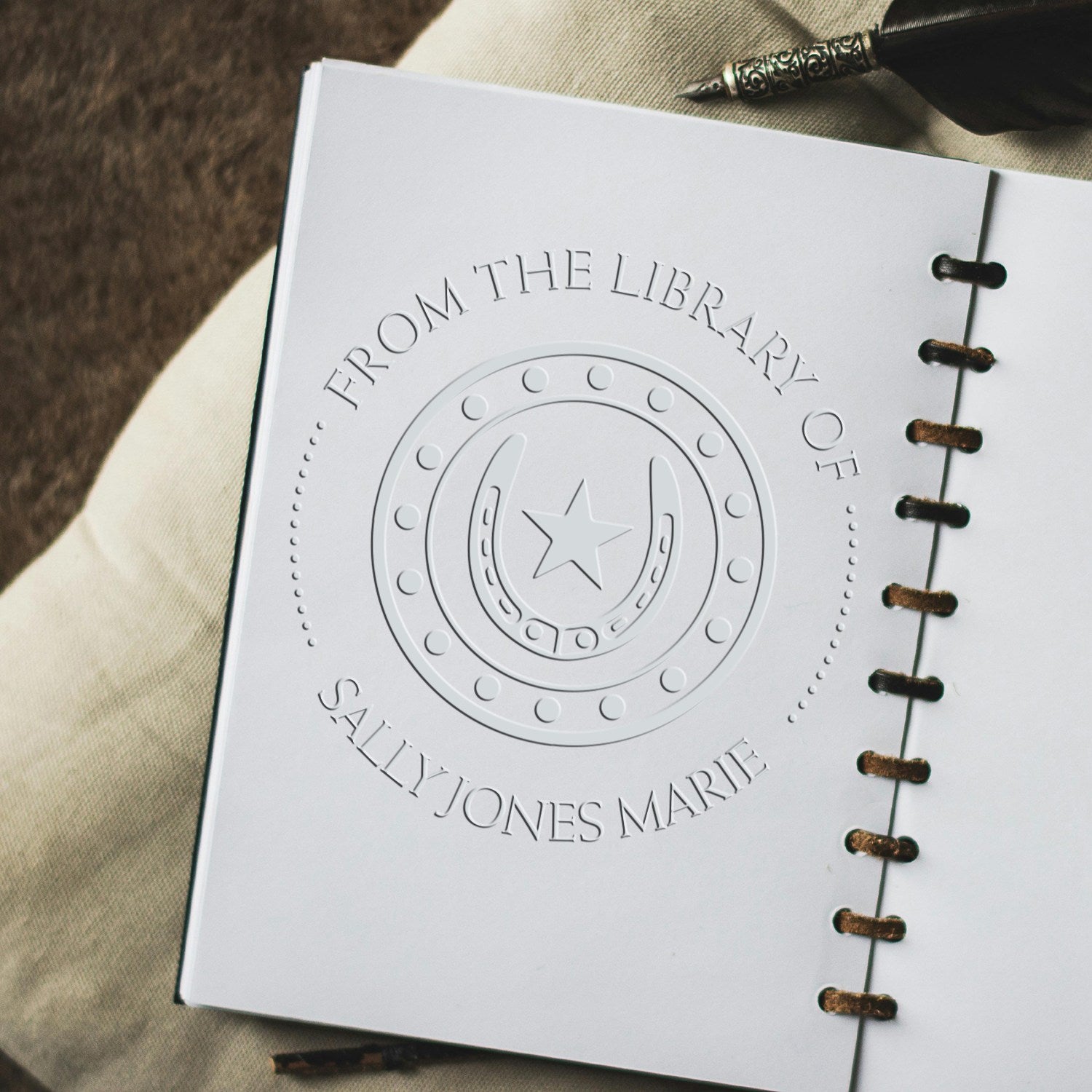White embossed custom library stamp seal with horseshoe and star on a spiral-bound notebook page.