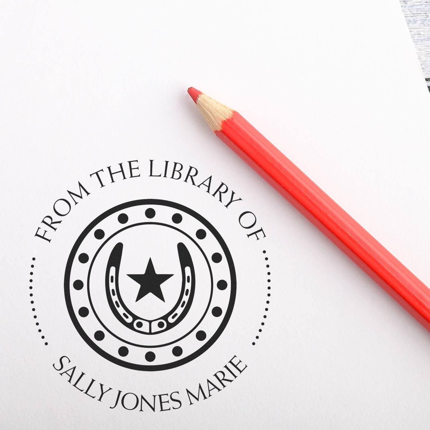 Black custom library stamp seal with horseshoe and star, paired with a red pencil on white paper.