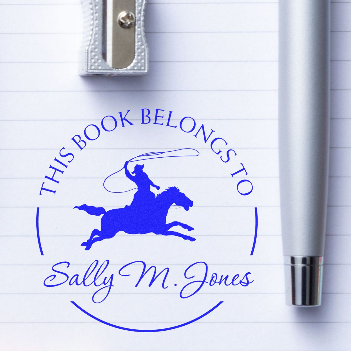 Blue custom book seal stamp on lined paper, featuring a horse-and-rider logo and Sally M. Jones, beside a silver stamp handle.