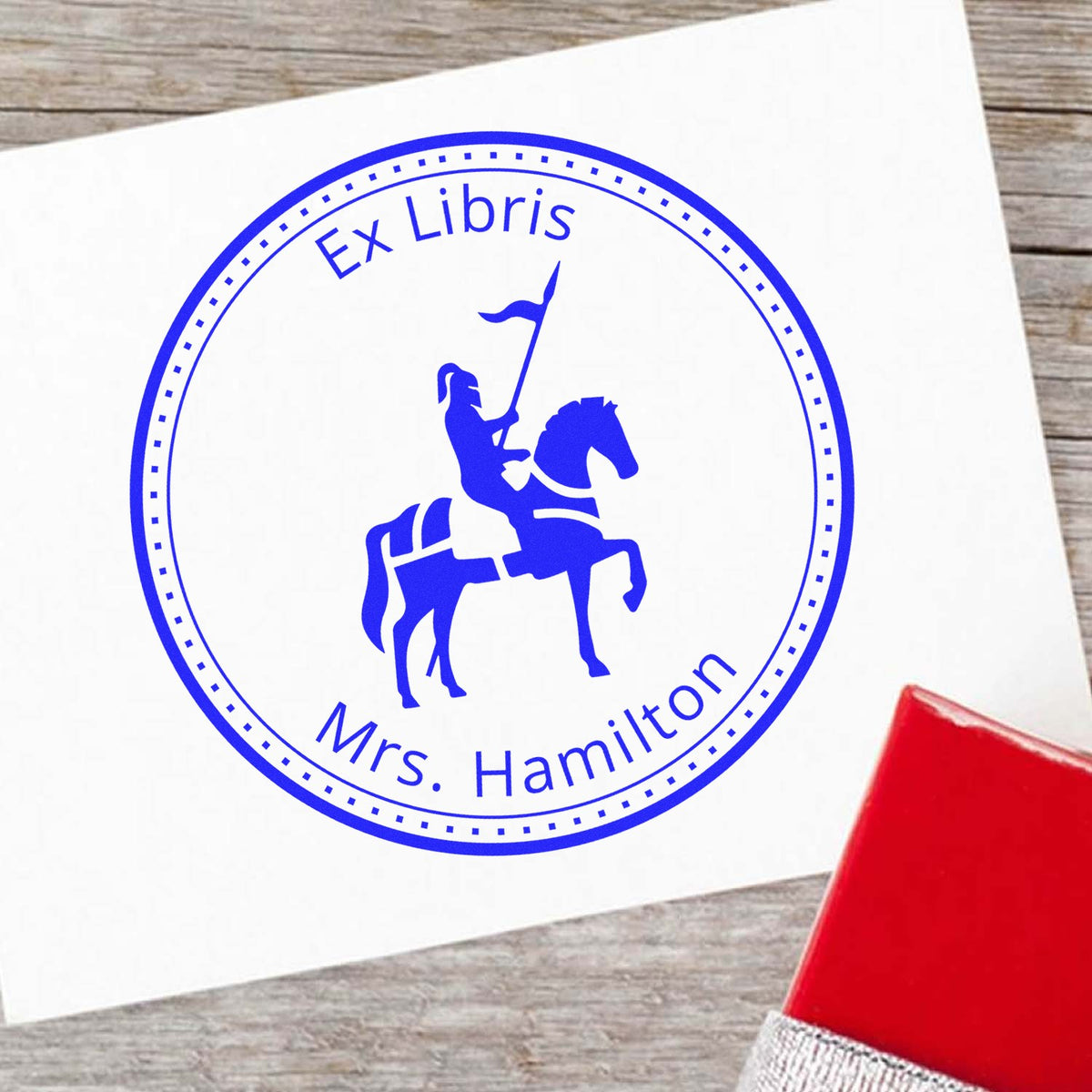 Blue circular Ex Libris stamp seal with knight on horseback and Mrs. Hamilton on white paper, beside a red stamp pad.