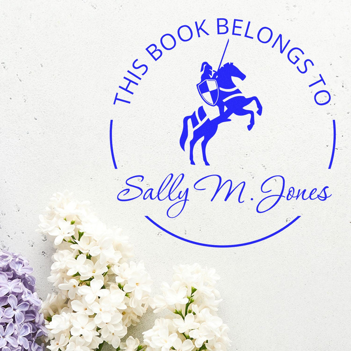 Blue custom book seal stamp with horse and rider, reading This Book Belongs to Sally M. Jones, on a white background with flowers.
