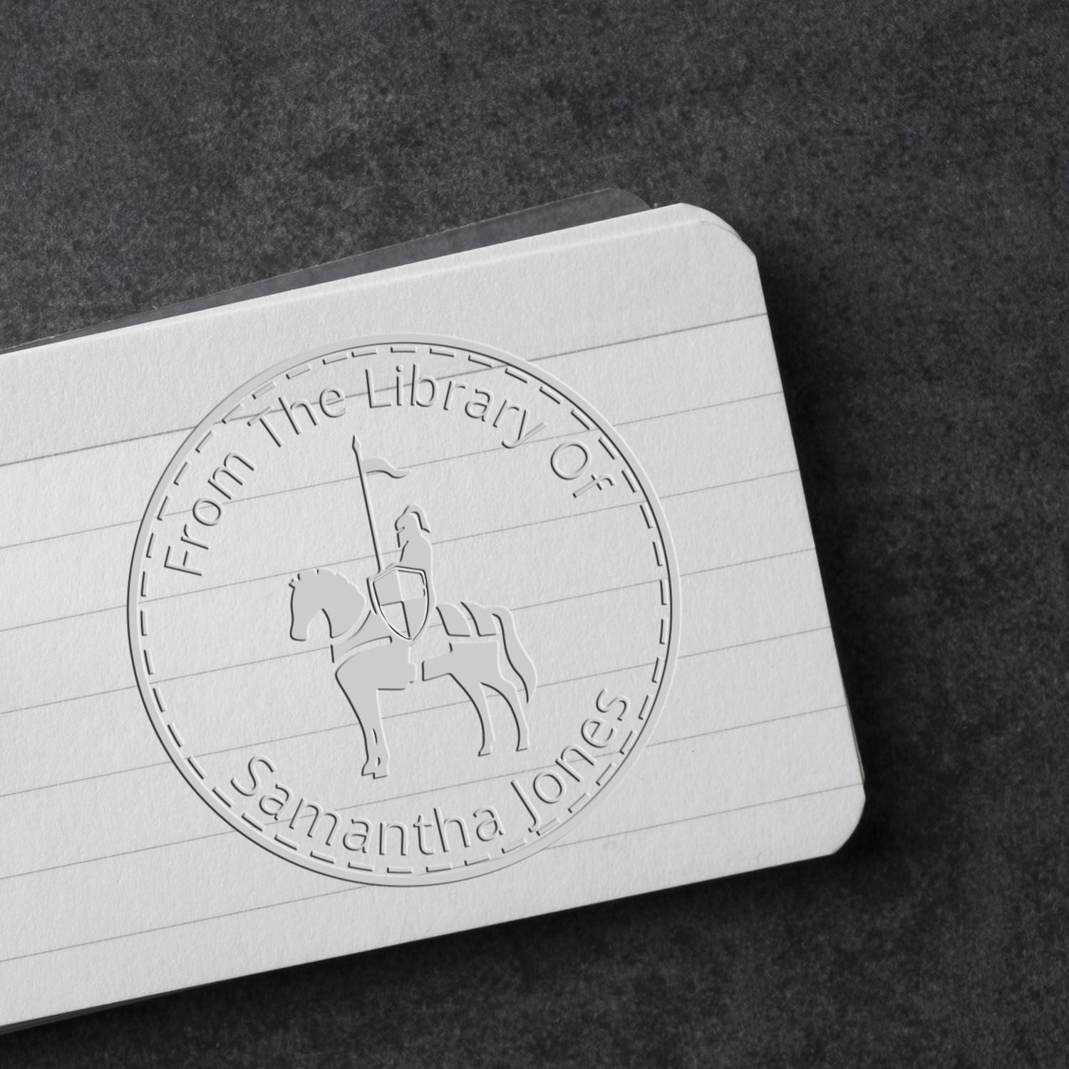 Embossed white library seal stamp on lined card, featuring a knight on horseback and the name Samantha Jones on a black background.