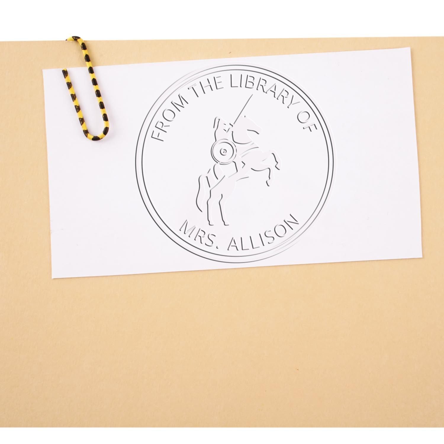 White paper featuring a black circular library stamp seal reading From the Library of Mrs. Allison, clipped with a yellow-black cord.