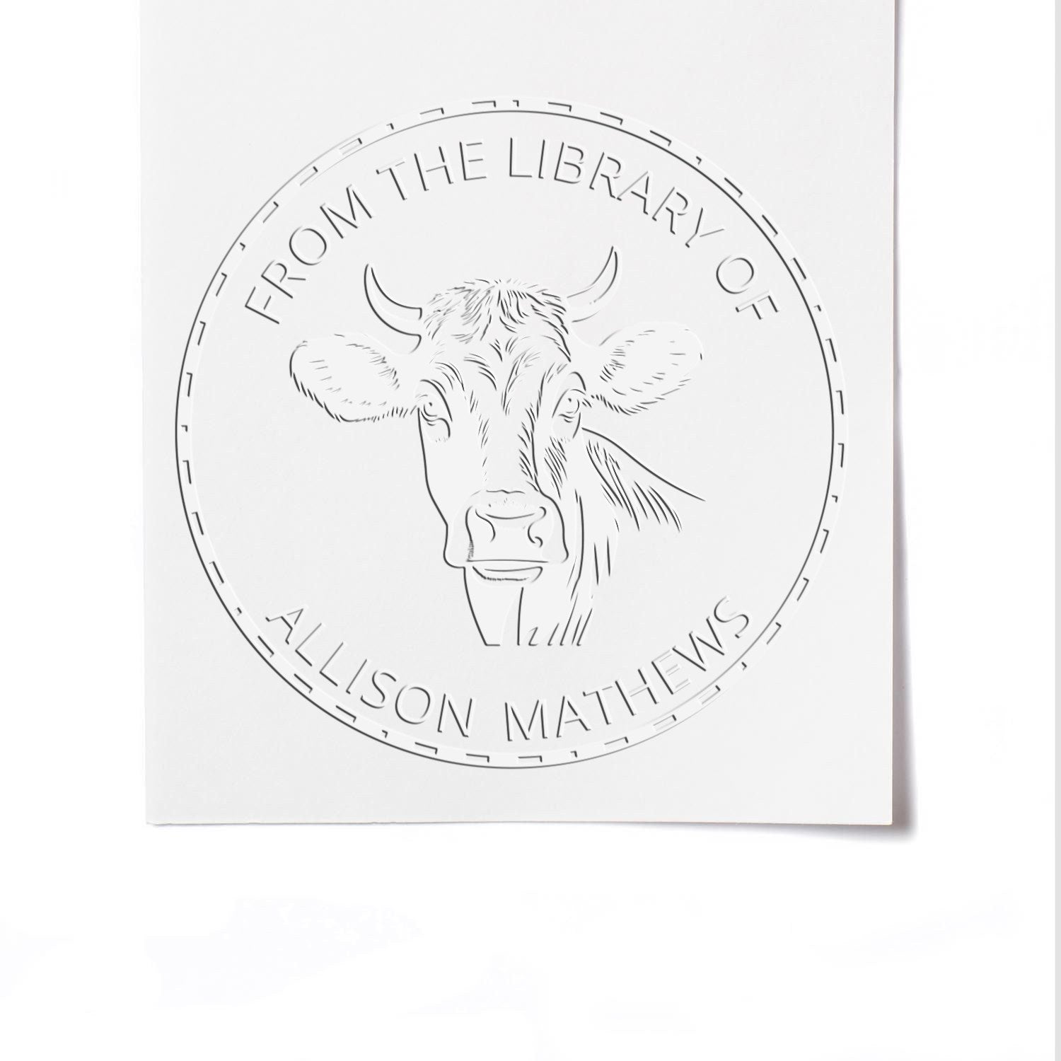 Embossed white library book seal stamp with cow head and circular text From the Library of Allison Mathews.
